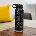 Black insulated water bottle engraved with a collage of video game icons — controllers, cartridges and arcade art — on a side table