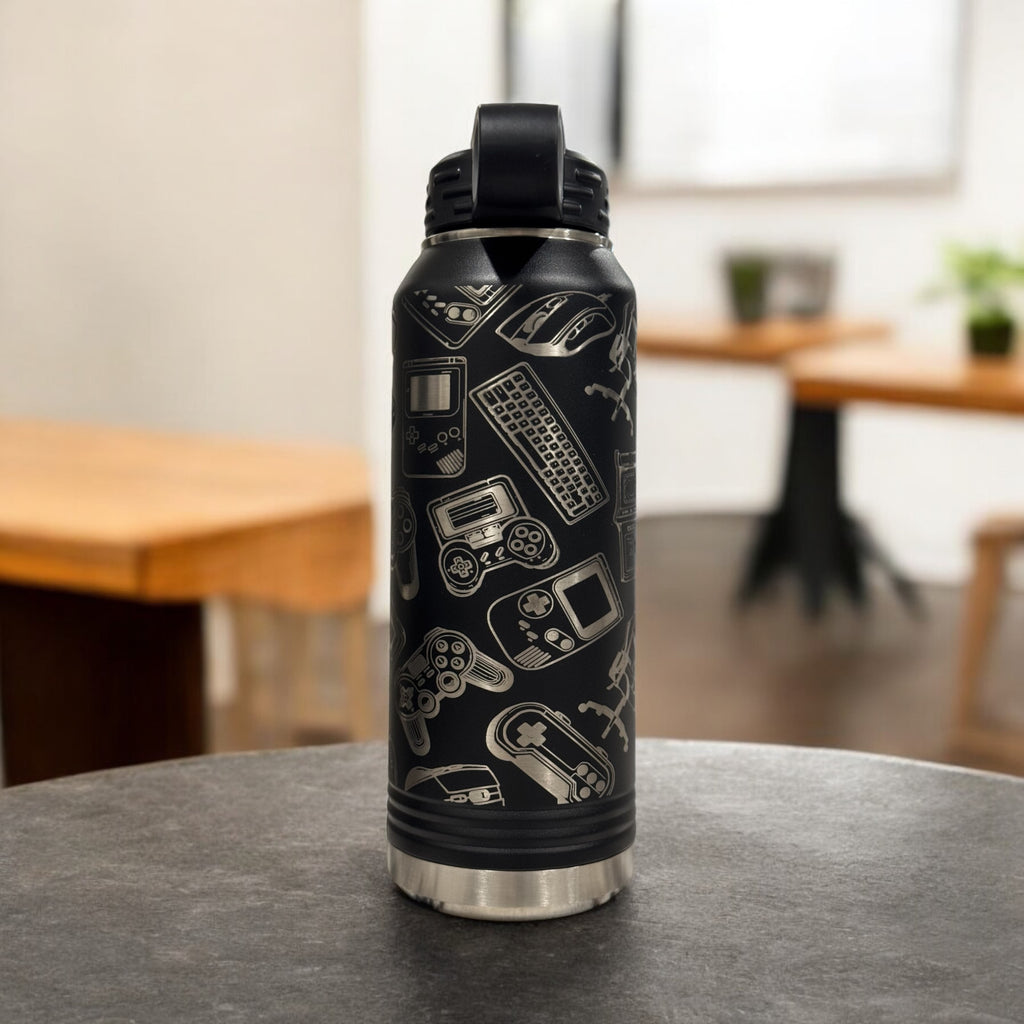 Black insulated water bottle engraved with a collage of video game icons, standing on a dining table