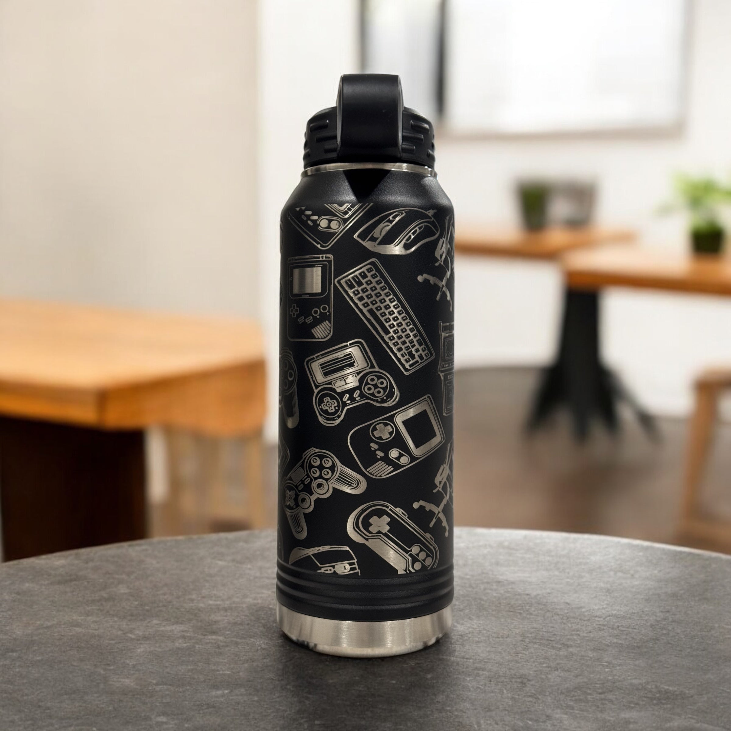 Black insulated water bottle engraved with a collage of video game icons, standing on a dining table