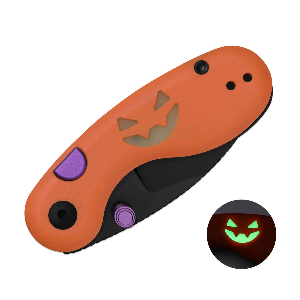 Kizer Microbe Halloween Edition closed, with the handle's jack-o'-lantern glowing in the dark