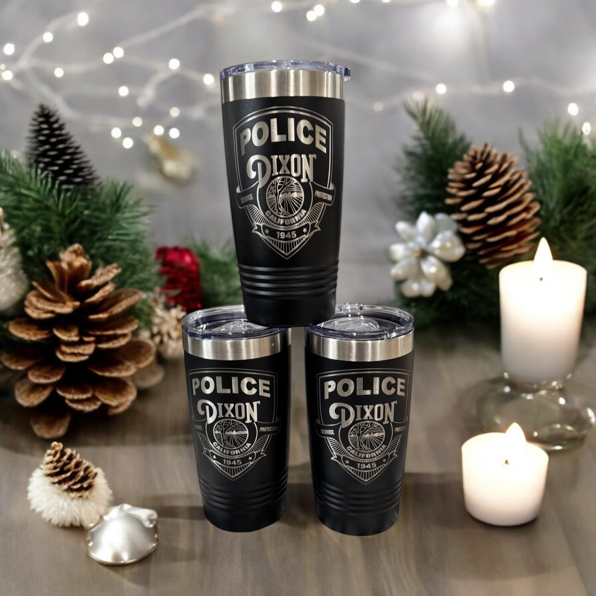 Three black 20 oz. ringneck tumblers laser engraved with a police department badge, styled with pine cones and candles