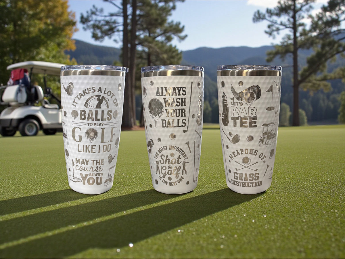 Three engraved tumblers with a golf design standing on a golf course fairway