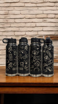 A row of black insulated water bottles engraved with a collage of video game icons, standing on a wooden table against a brick wall