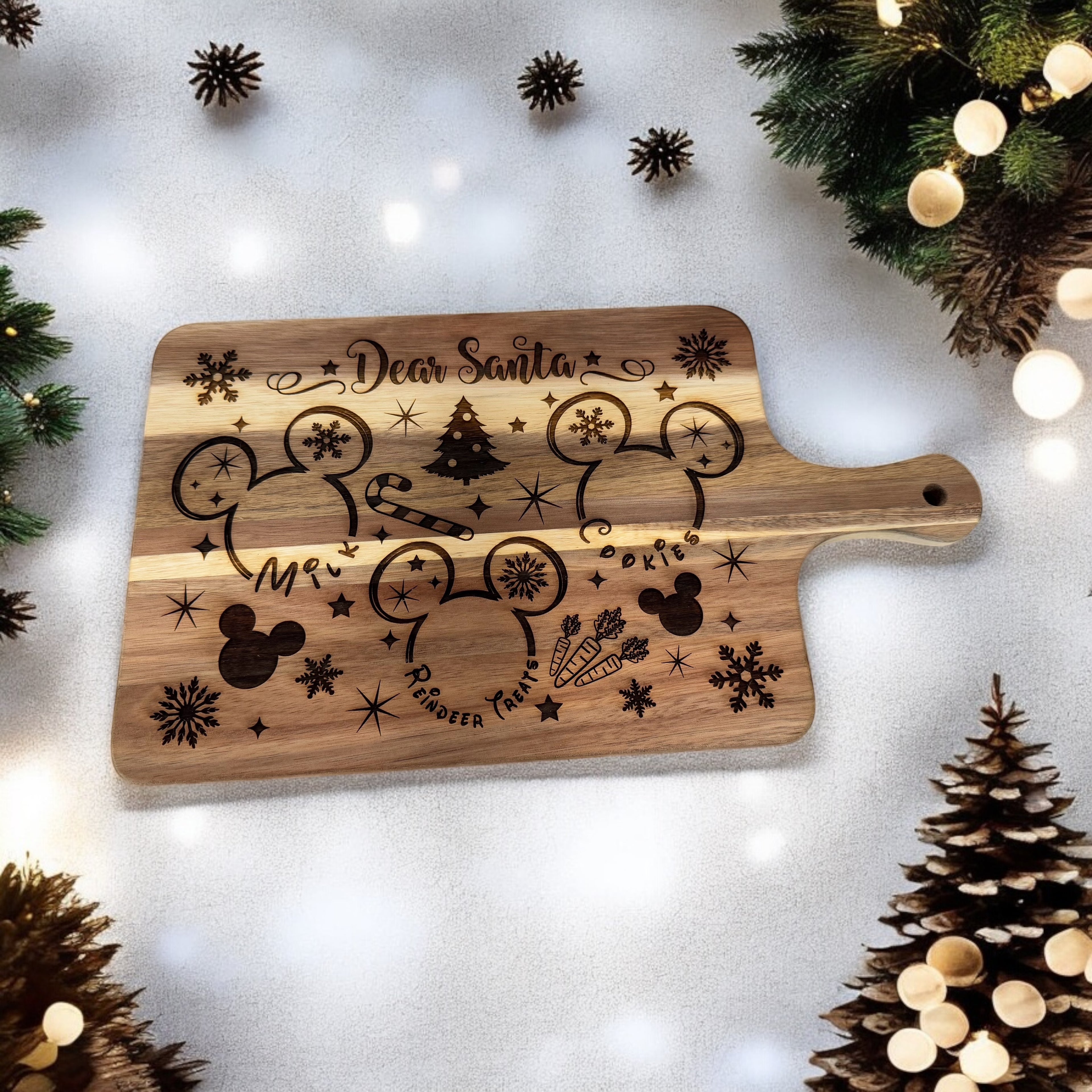 Engraved wooden Santa treat tray with a paddle handle, staged with miniature Christmas trees and greenery