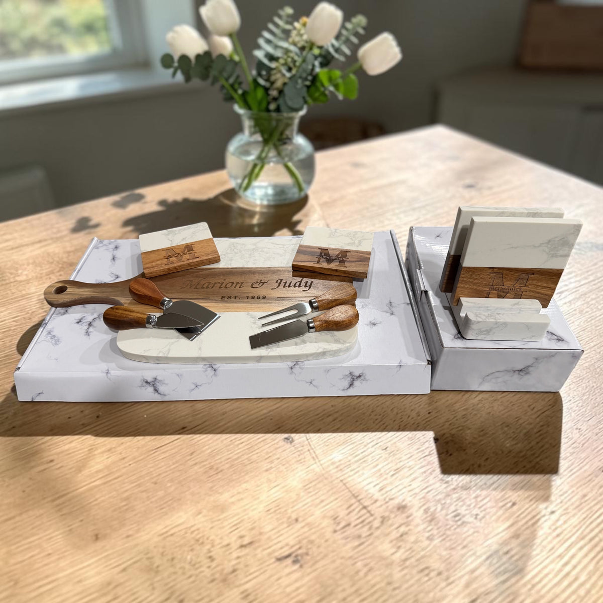 Marble and acacia serving board engraved with a couple's names and anniversary year, laid out with cheese tools and the monogrammed coaster set