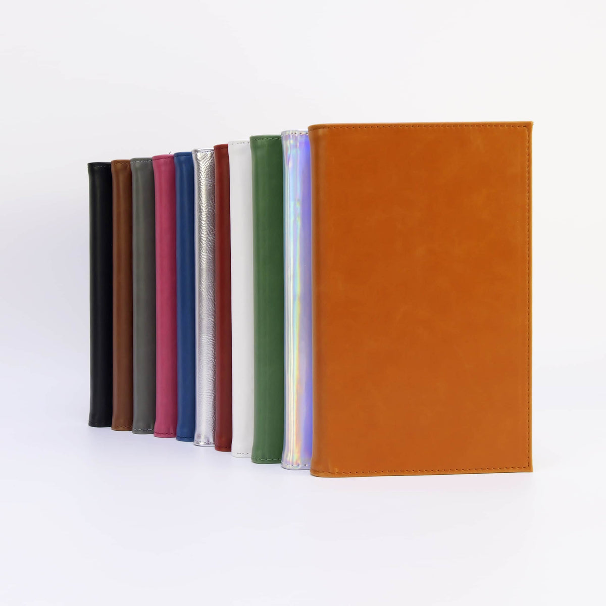 Twelve leatherette journal colors standing in a row with a rawhide tan journal in front