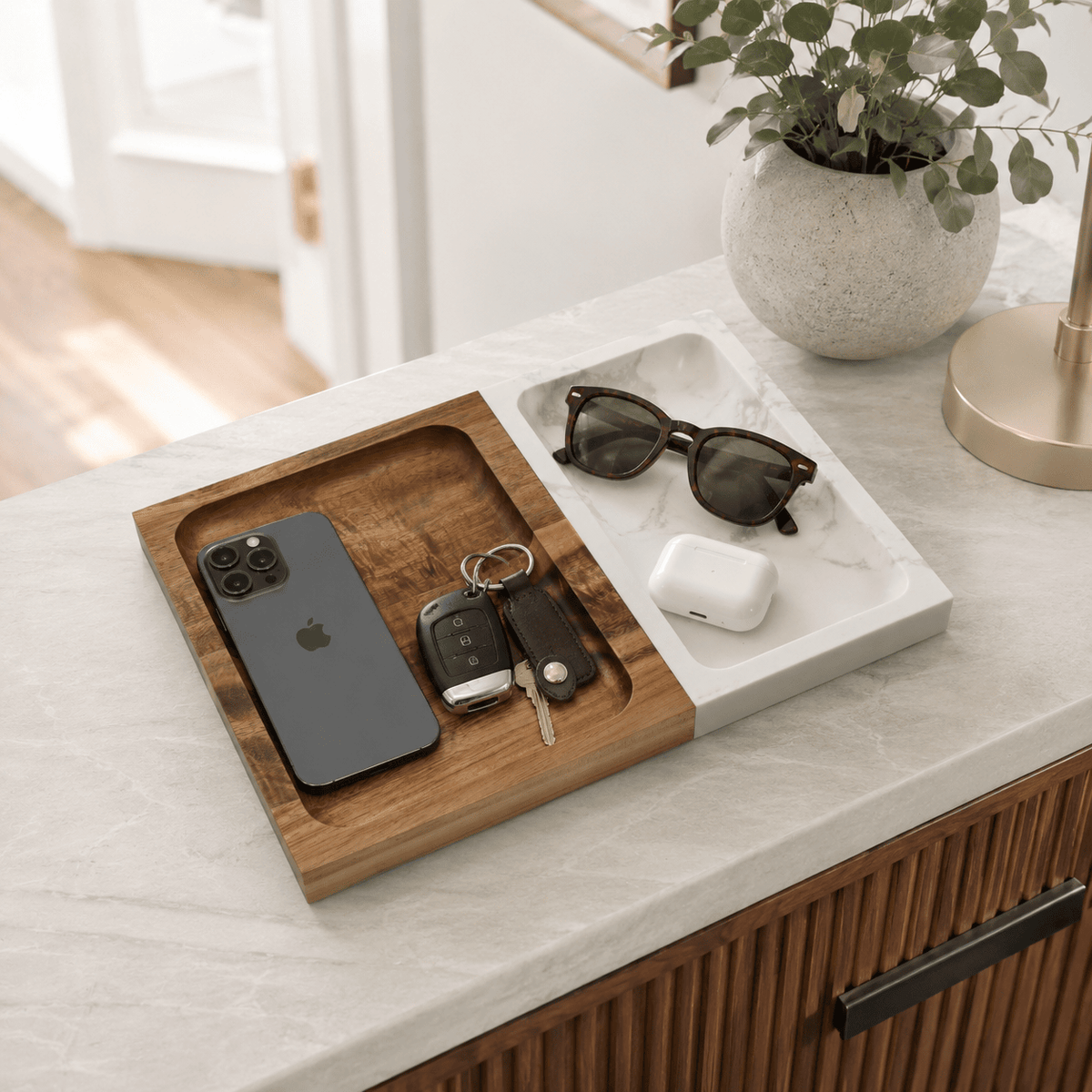 Marble and wood valet tray on a kitchen counter holding a phone, car keys, sunglasses and earbuds