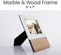 Marble and acacia wood 5x7 picture frame standing at an angle with a wedding photo in it, black fold-out stand visible behind