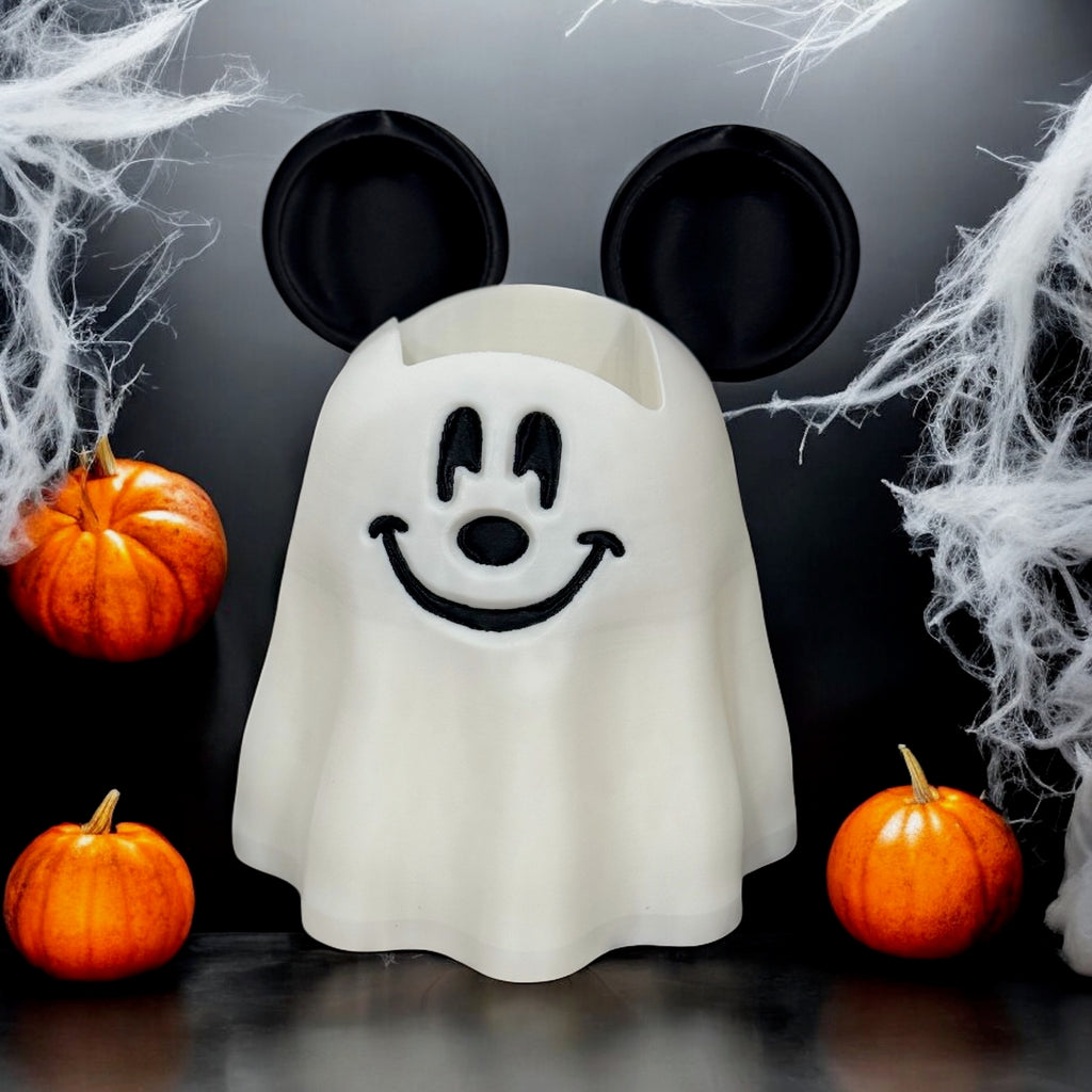 White ghost-shaped soap dispenser cover with mouse ears, photographed against a black cobweb backdrop with pumpkins