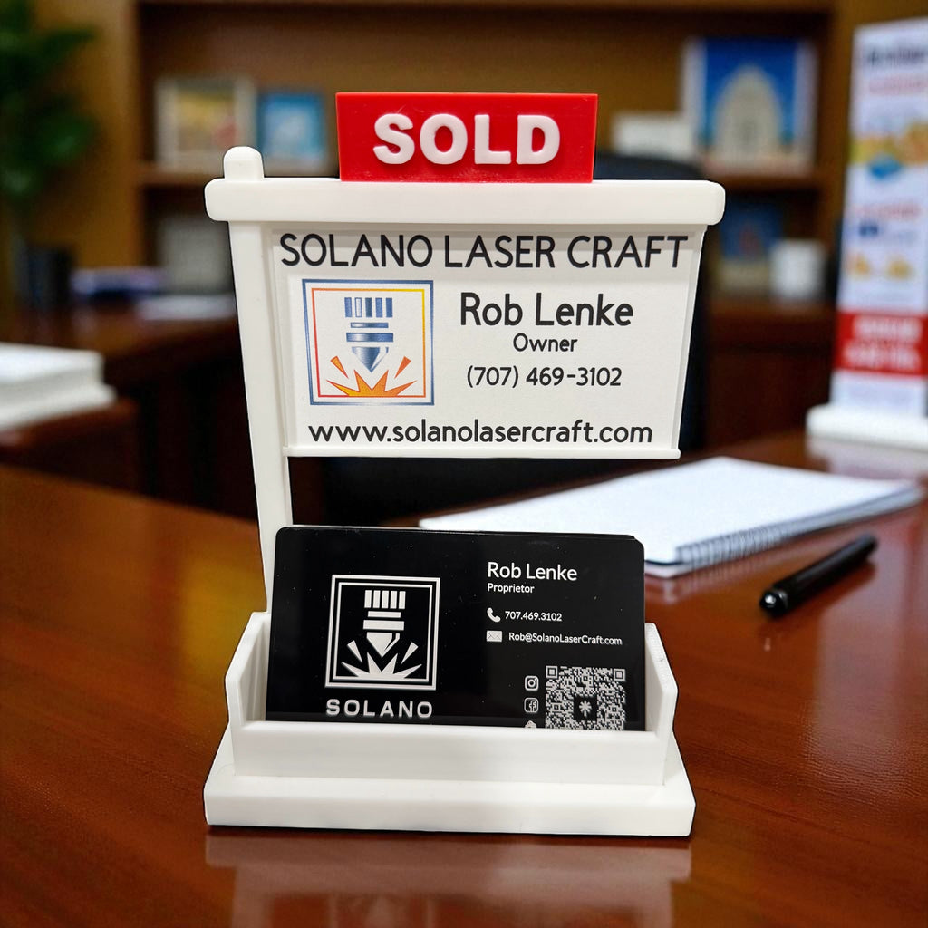 Miniature real estate yard sign business card holder with a SOLD rider, holding a Solano Laser Craft business card