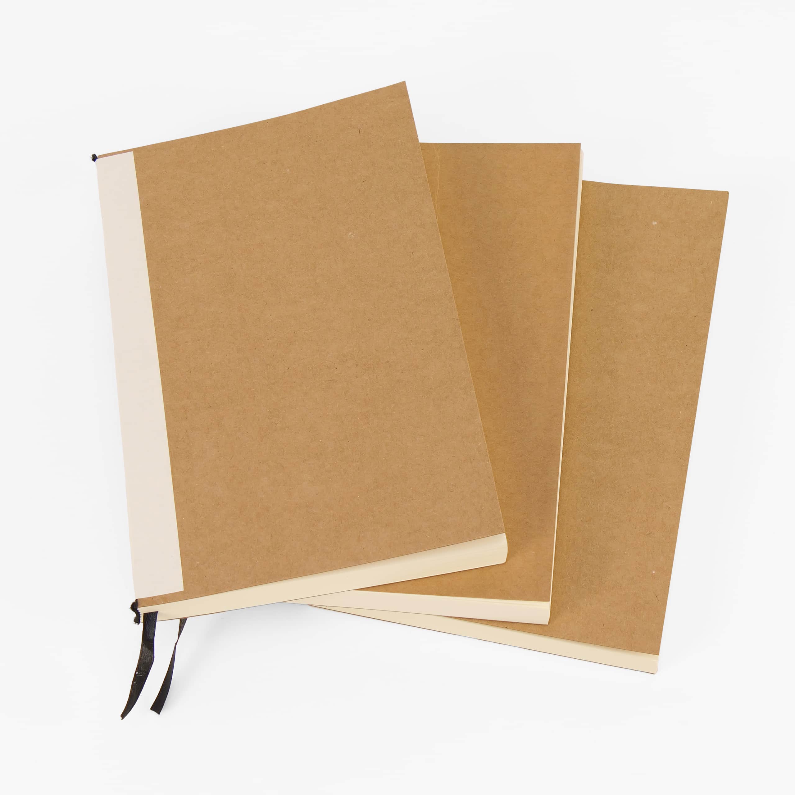 Three kraft-cover journal refill notebooks fanned out, the front one showing its black ribbon bookmark