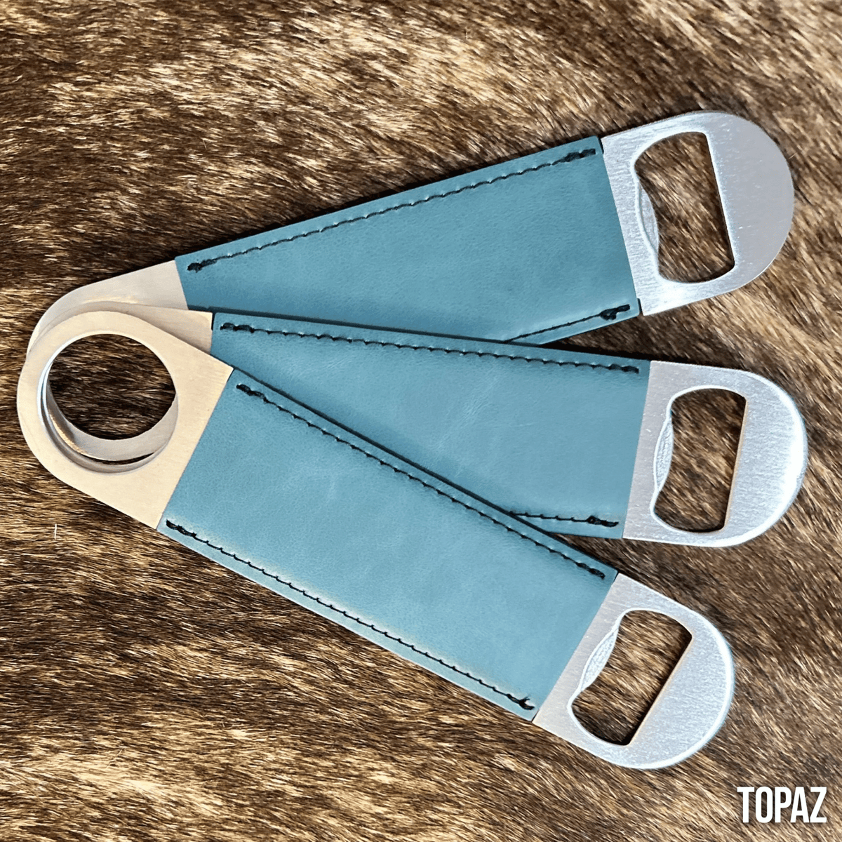Three stainless steel bar bottle openers wrapped in Topaz blue Premium Leatherette, fanned out to show the wrap and the opener end.