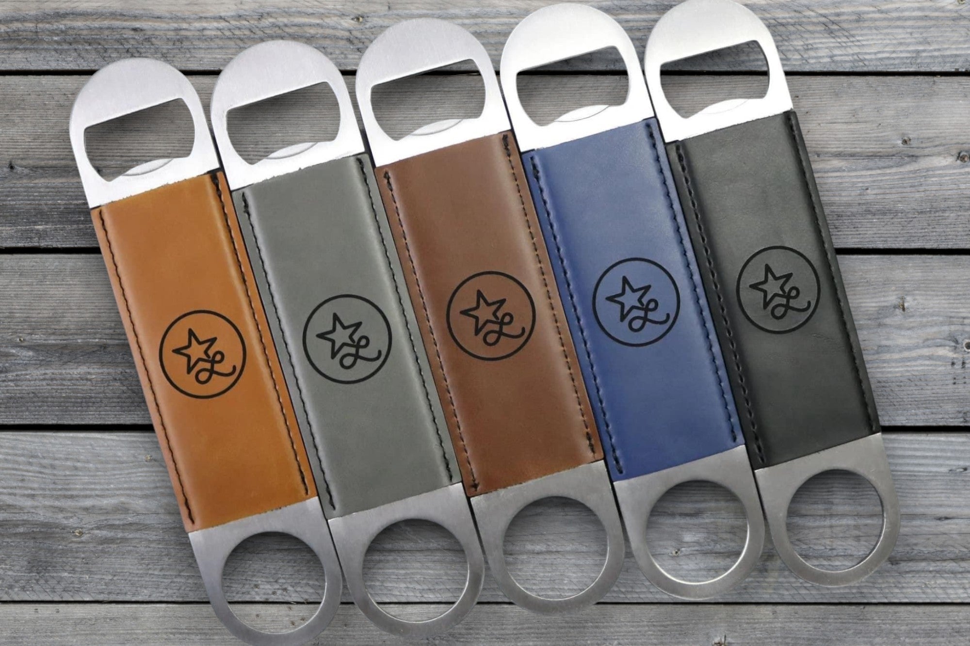 Five Premium Leatherette bottle openers in tan, grey, olive, blue and dark brown fanned across weathered wood, each laser engraved with a sample design.