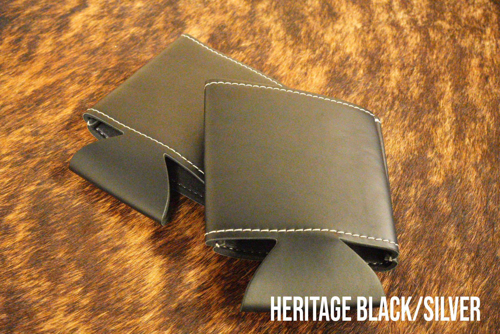 Black Premium Leatherette can coolers that engrave to silver, shown folded on a cowhide surface.