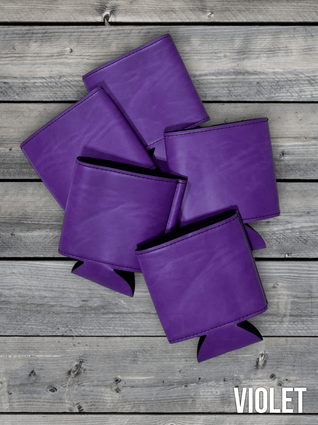 Several Violet purple Premium Leatherette can coolers laid flat on weathered wood, shown collapsed.