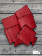 Several Ruby red Premium Leatherette can coolers laid flat on weathered wood, shown collapsed.