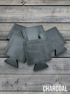 Several Charcoal grey Premium Leatherette can coolers laid flat on weathered wood, shown collapsed.