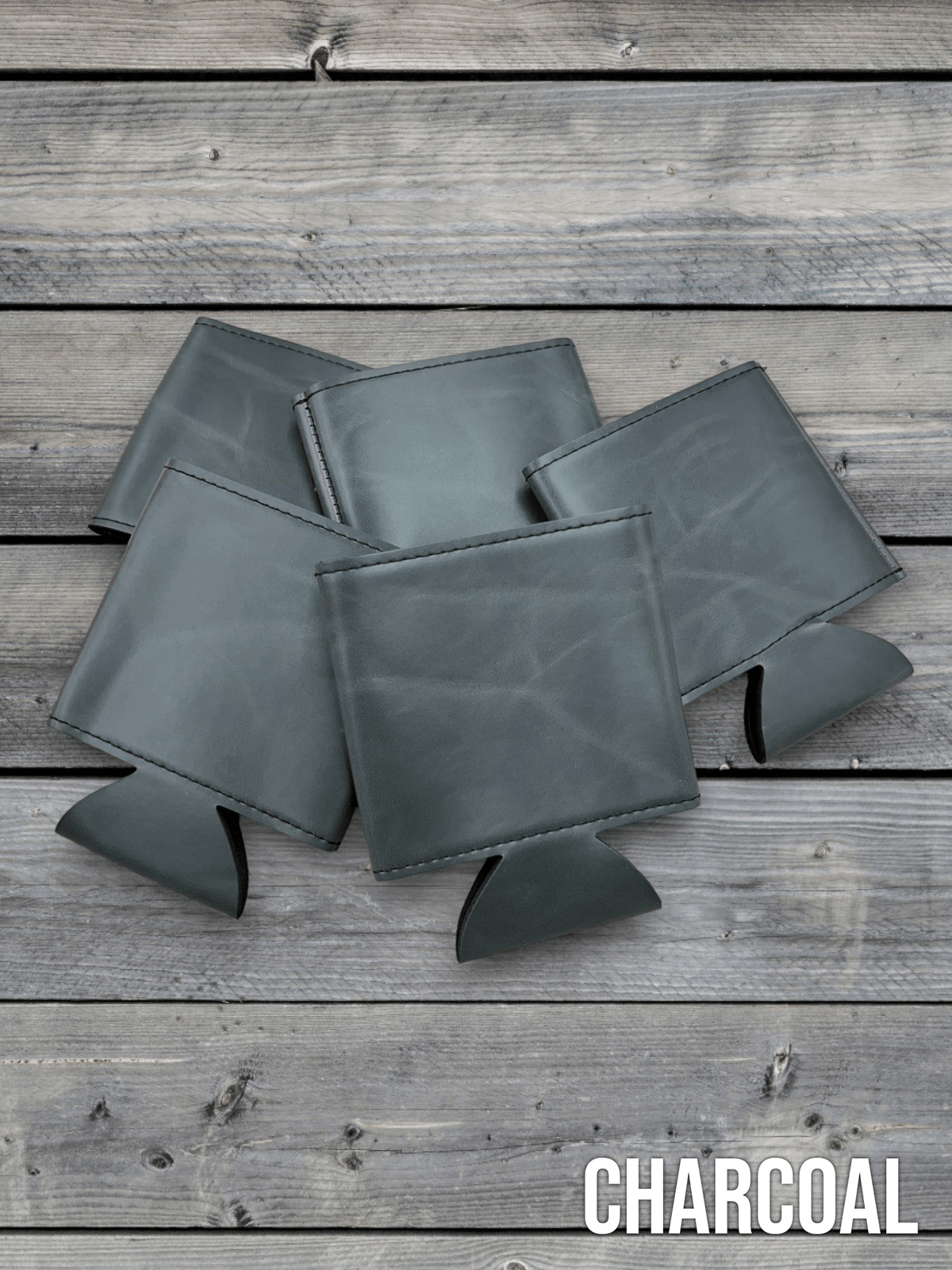 Several Charcoal grey Premium Leatherette can coolers laid flat on weathered wood, shown collapsed.