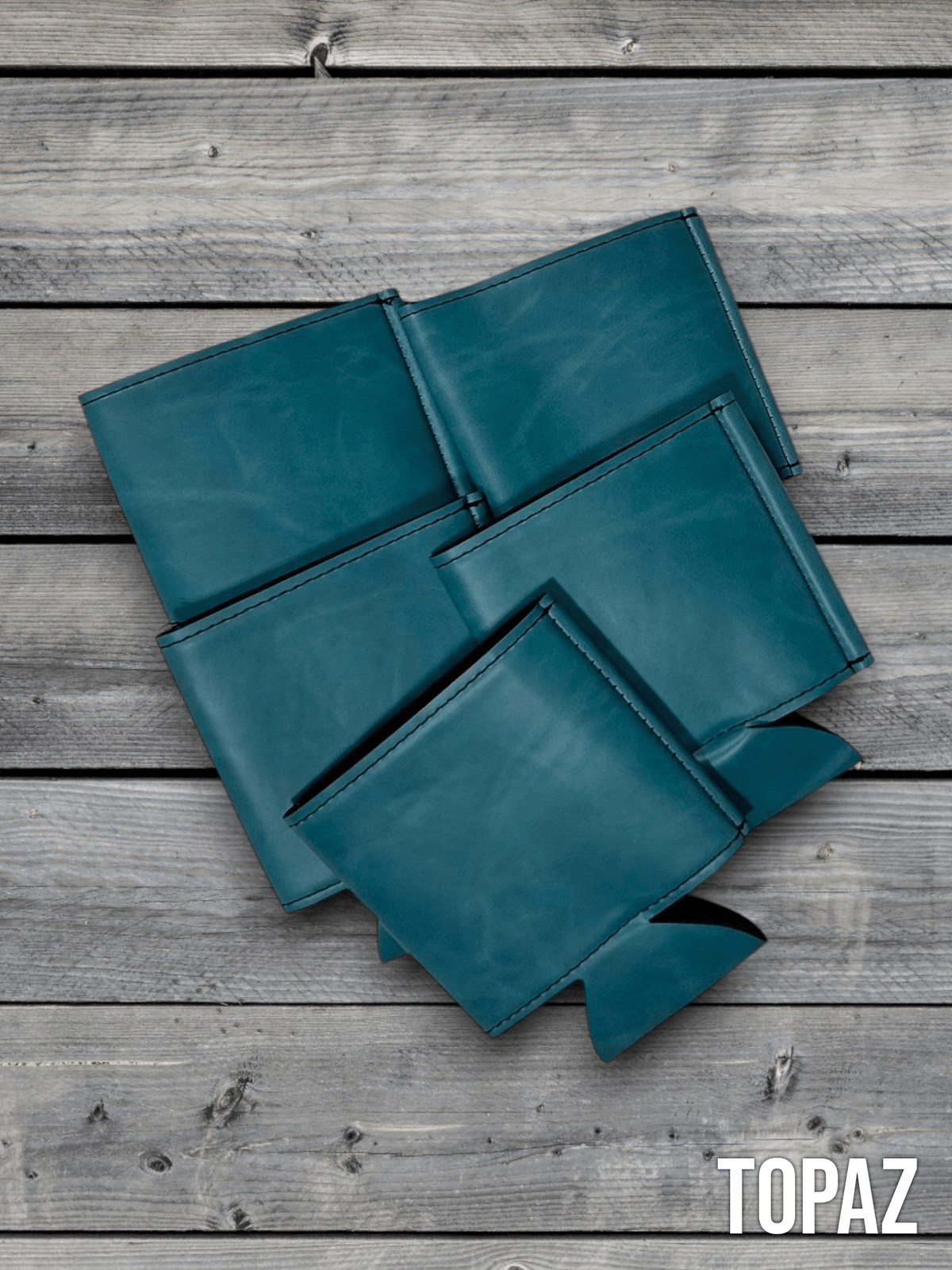 Several Topaz teal Premium Leatherette can coolers laid flat on weathered wood, shown collapsed.