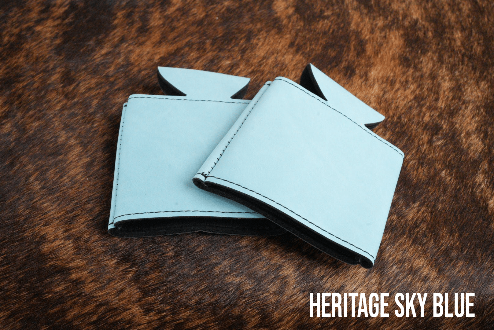 Several Sky Blue Premium Leatherette can coolers laid flat on weathered wood, shown collapsed.