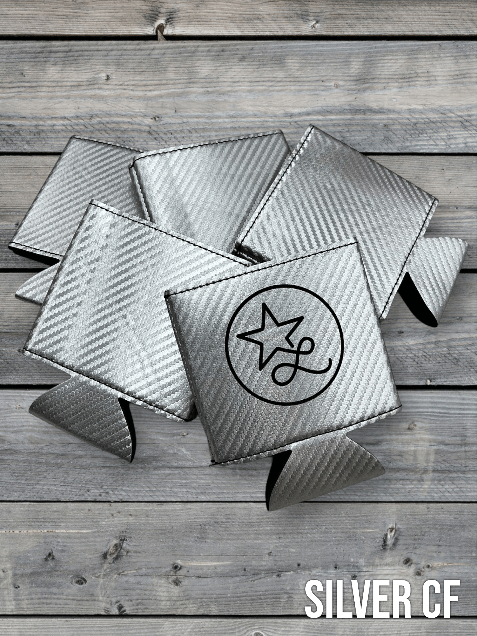 Silver carbon fiber Premium Leatherette can coolers with a woven texture, shown folded on a cowhide surface.