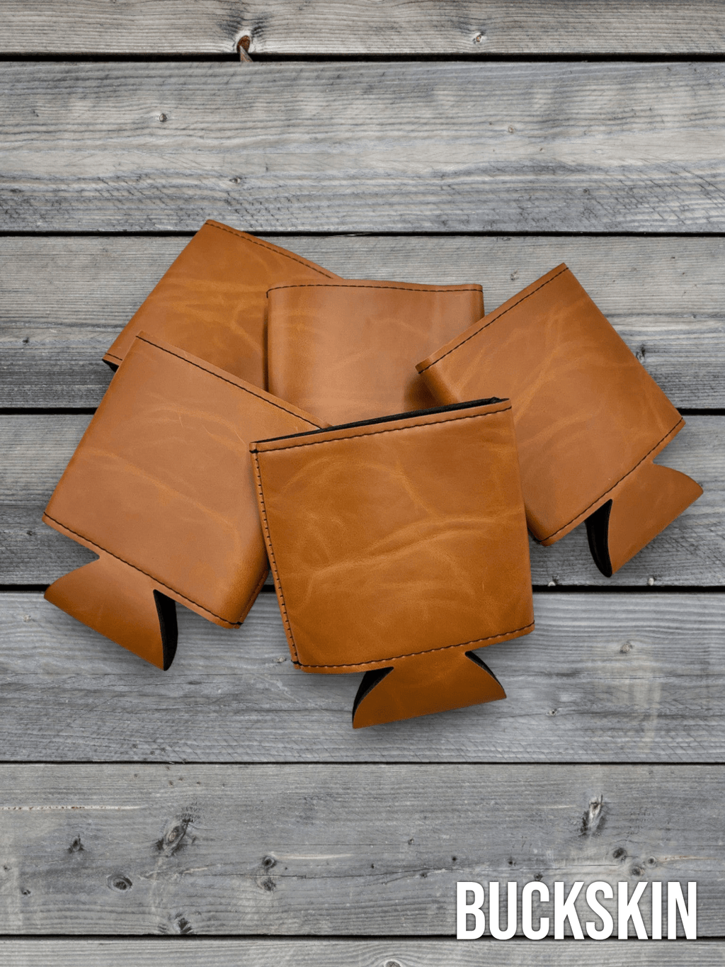 Several Buckskin tan Premium Leatherette can coolers laid flat on weathered wood, shown collapsed.