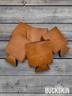 Several Buckskin tan Premium Leatherette can coolers laid flat on weathered wood, shown collapsed.