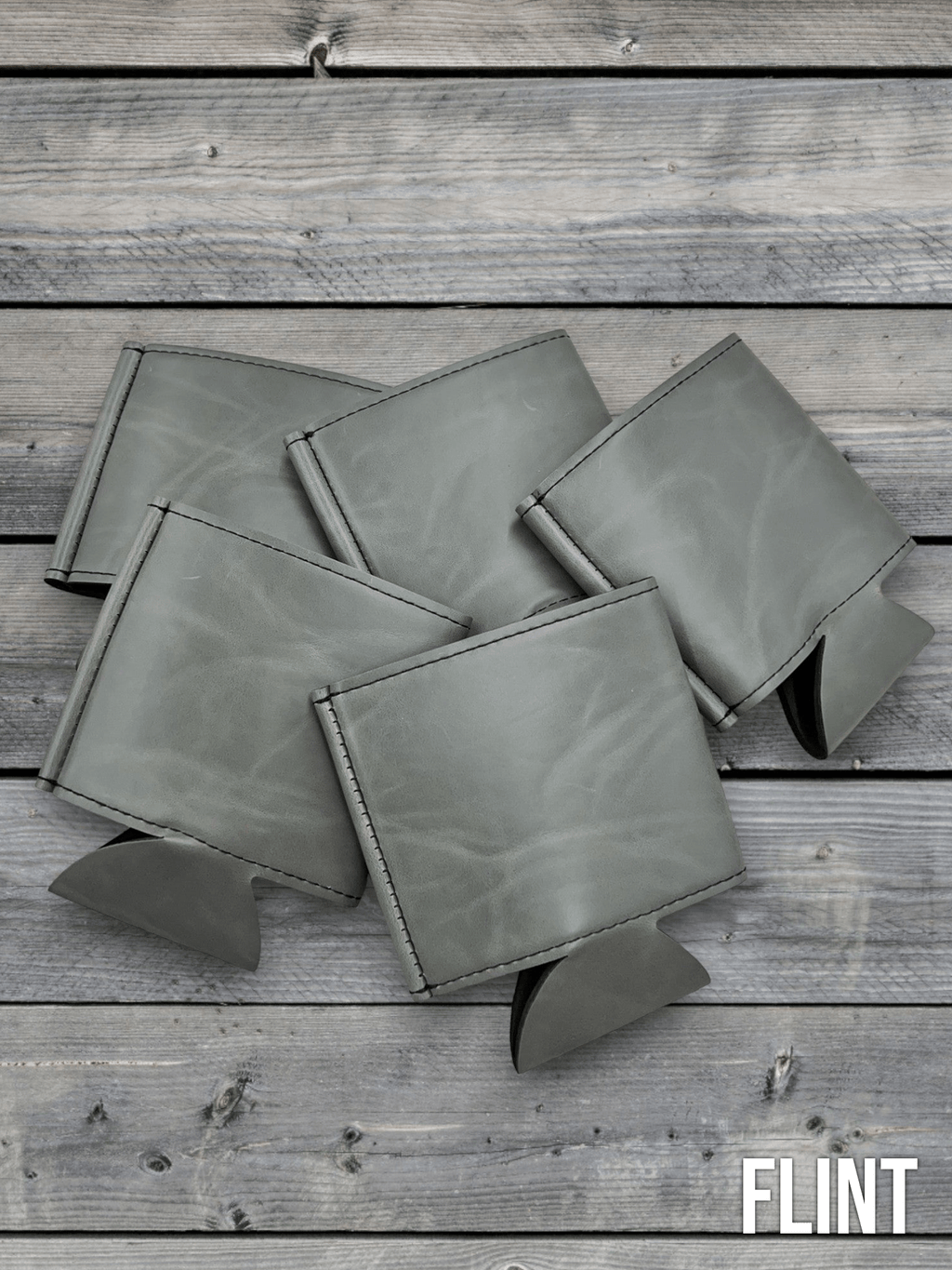 Several Flint grey Premium Leatherette can coolers laid flat on weathered wood, shown collapsed.