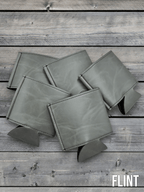 Several Flint grey Premium Leatherette can coolers laid flat on weathered wood, shown collapsed.