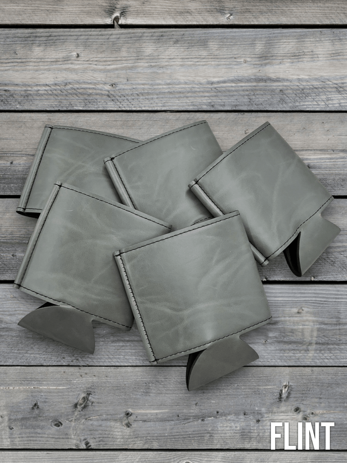 Several Flint grey Premium Leatherette can coolers laid flat on weathered wood, shown collapsed.