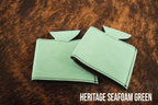 Several Sea Foam mint green Premium Leatherette can coolers laid flat on weathered wood, shown collapsed.