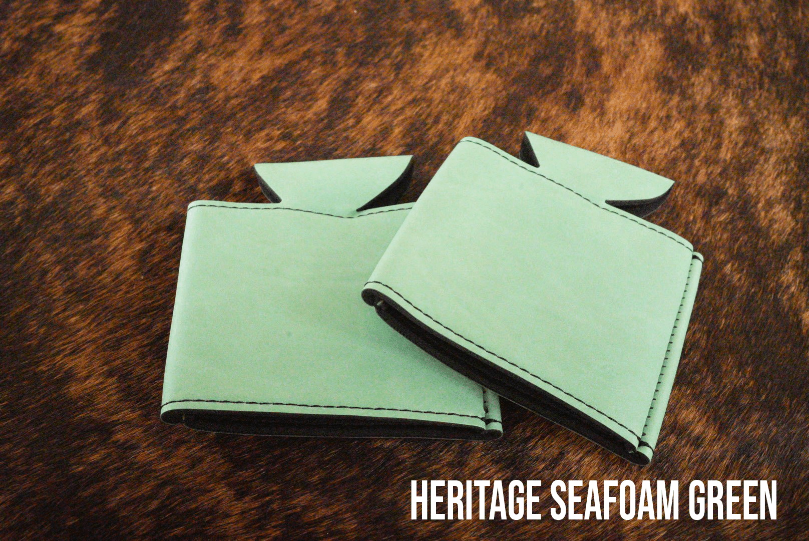Several Sea Foam mint green Premium Leatherette can coolers laid flat on weathered wood, shown collapsed.