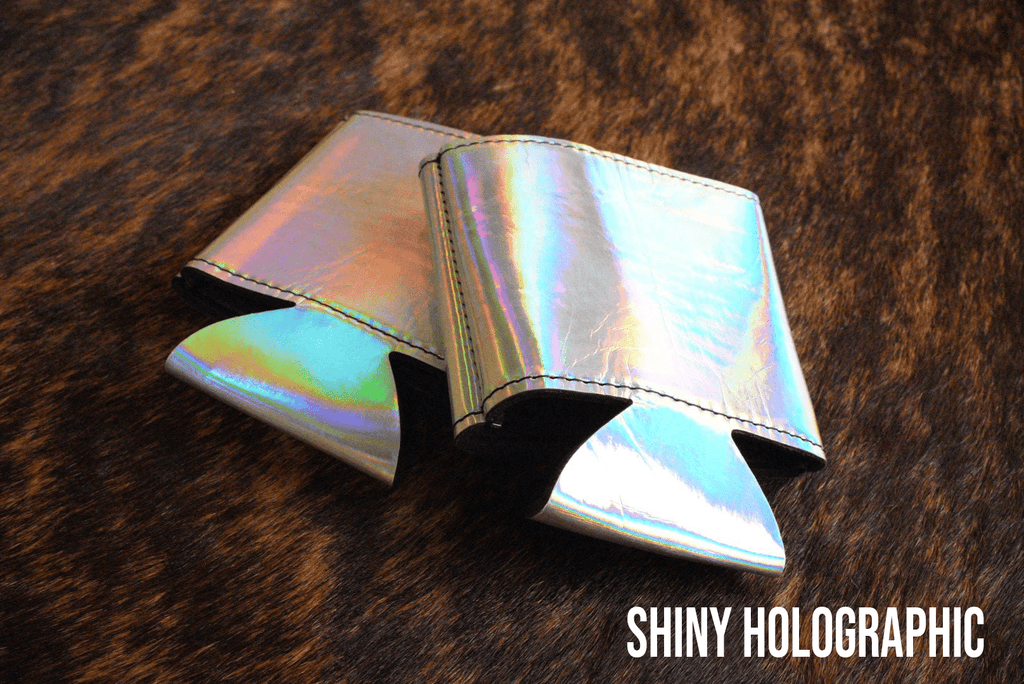 Shiny holographic Premium Leatherette can coolers with a bright iridescent finish, laid flat and collapsed.