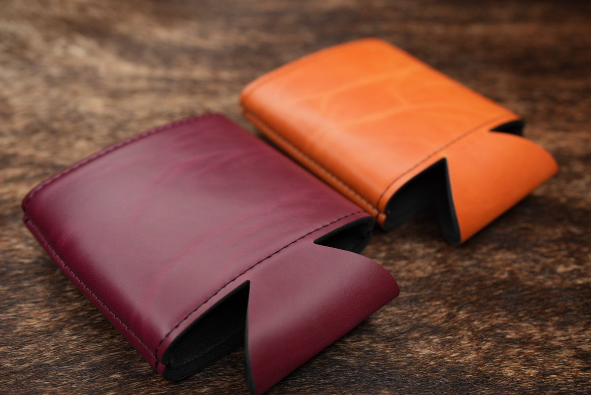 Maroon and orange Premium Leatherette can coolers lying collapsed on a weathered wood surface.
