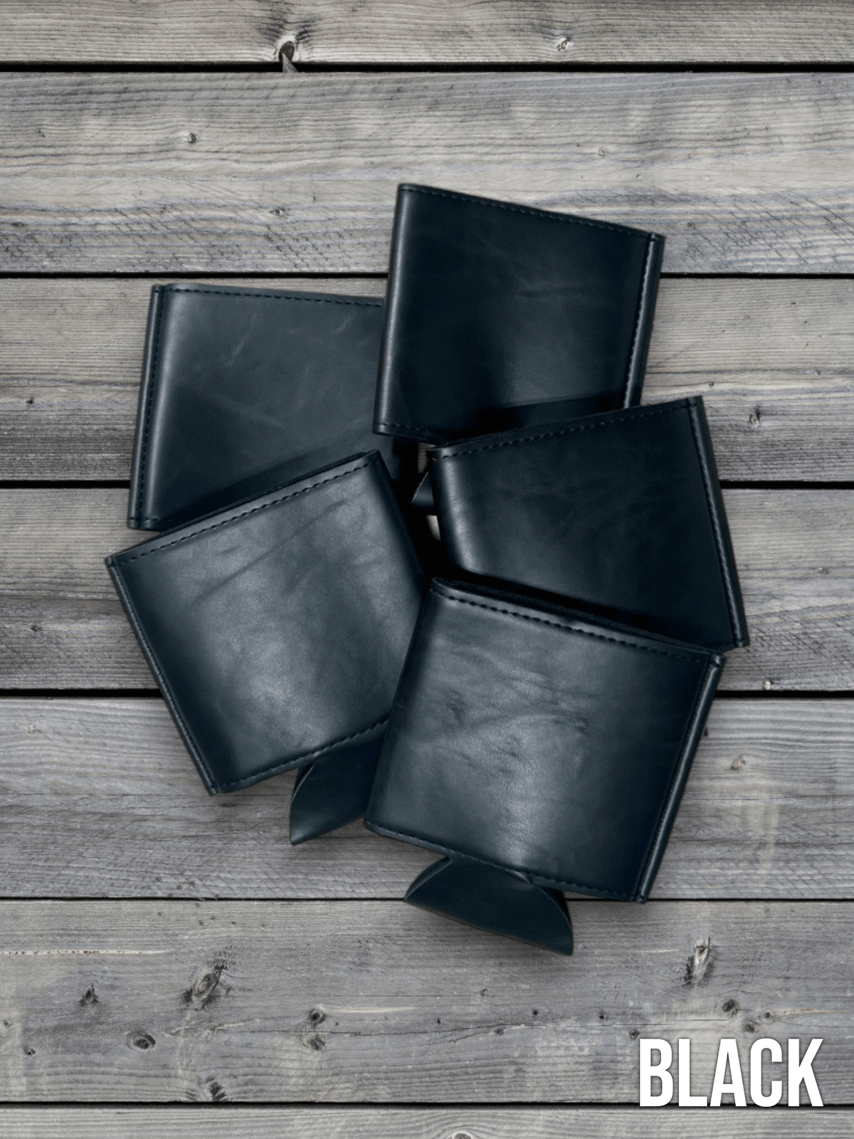Several Black Premium Leatherette can coolers laid flat on weathered wood, shown collapsed.