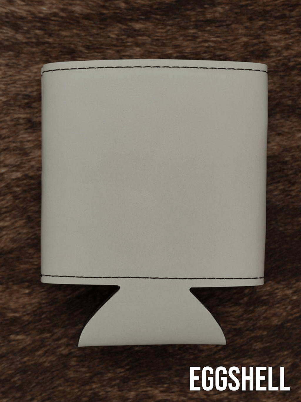 An Eggshell cream Premium Leatherette can cooler photographed upright on a cowhide surface.
