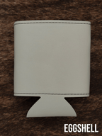 An Eggshell cream Premium Leatherette can cooler photographed upright on a cowhide surface.