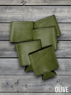 Several Olive green Premium Leatherette can coolers laid flat on weathered wood, shown collapsed.