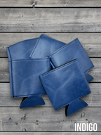 Several Indigo blue Premium Leatherette can coolers laid flat on weathered wood, shown collapsed.