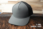 Charcoal and black Durra-Bull performance hat, five-panel, resting on a cowhide surface.