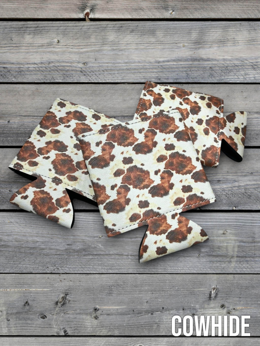 Cowhide print Premium Leatherette can coolers in a black and white hide pattern, laid flat and collapsed.