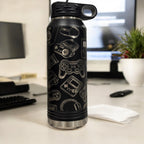 Black insulated water bottle engraved with a collage of video game icons, standing on a desk beside a keyboard and monitor