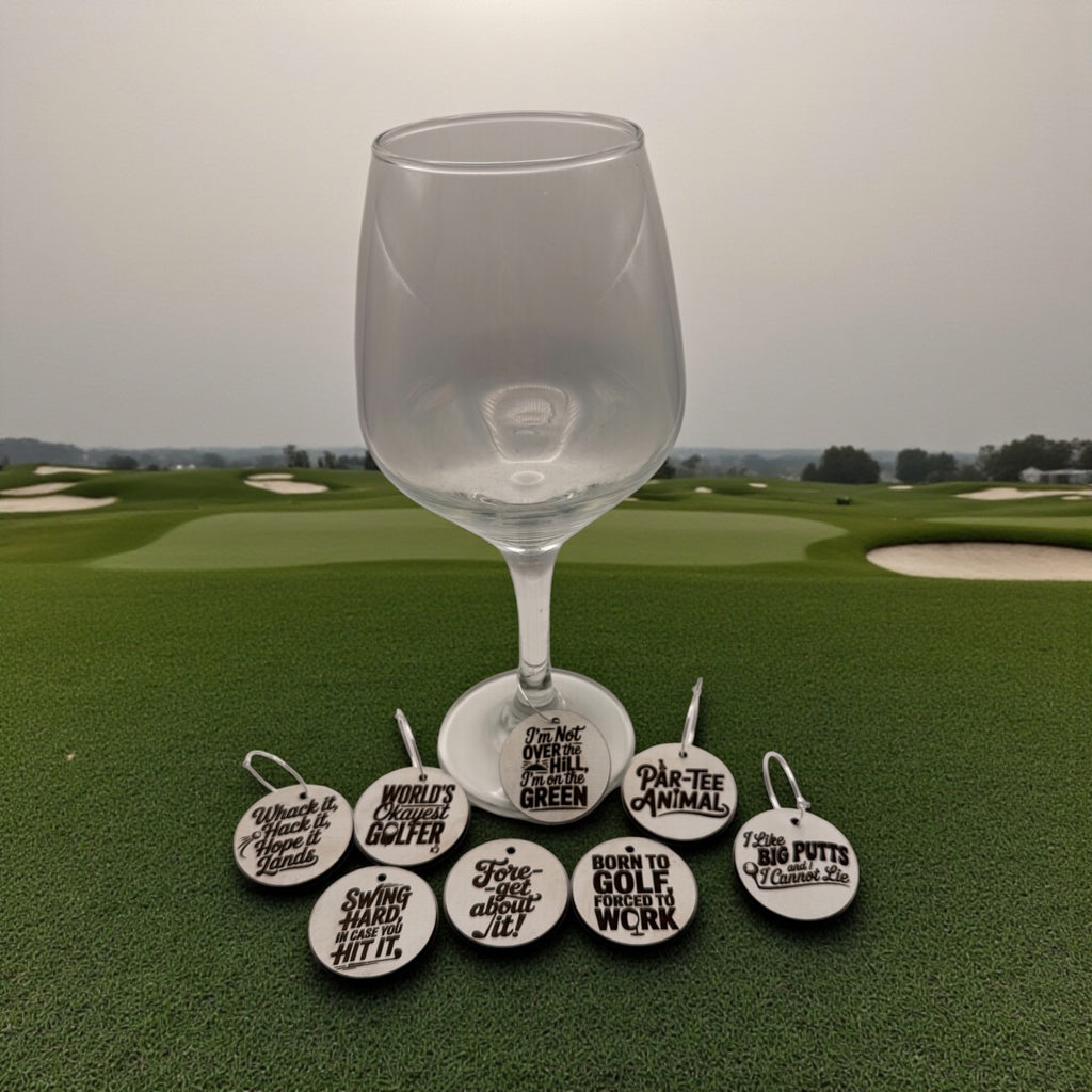 A wine glass on a golf course with a set of round wooden golf-themed wine charms laid out below it