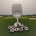 A wine glass on a golf course with a set of round wooden golf-themed wine charms laid out below it