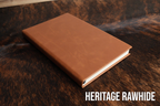 Heritage Rawhide Premium Leatherette journal cover, shown closed on a cowhide surface