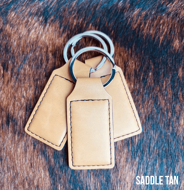 Three Saddle Tan Premium Leatherette keychains fanned out on a split ring, showing the blank engraving panel.