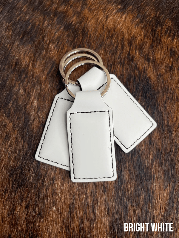 Three Bright White Premium Leatherette keychains fanned out on a split ring, showing the blank engraving panel.