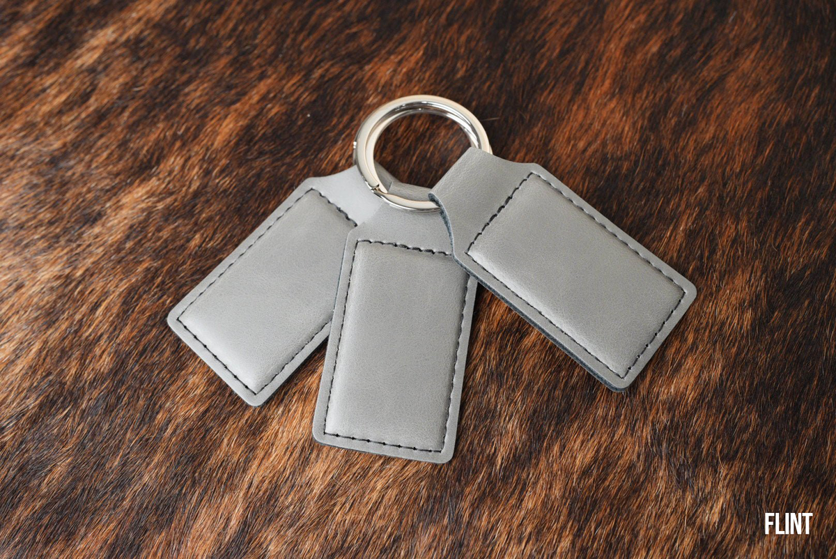Three Flint light grey Premium Leatherette keychains fanned out on a split ring, showing the blank engraving panel.