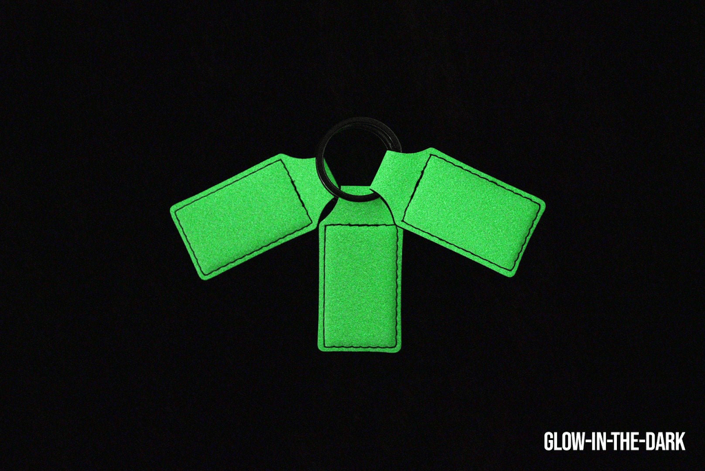 Three glow-in-the-dark Premium Leatherette keychains fanned out on a split ring, photographed glowing green in the dark.