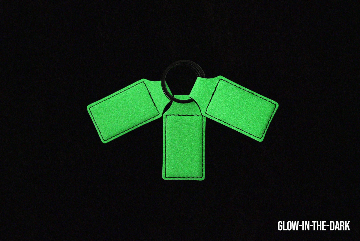 Three glow-in-the-dark Premium Leatherette keychains fanned out on a split ring, photographed glowing green in the dark.